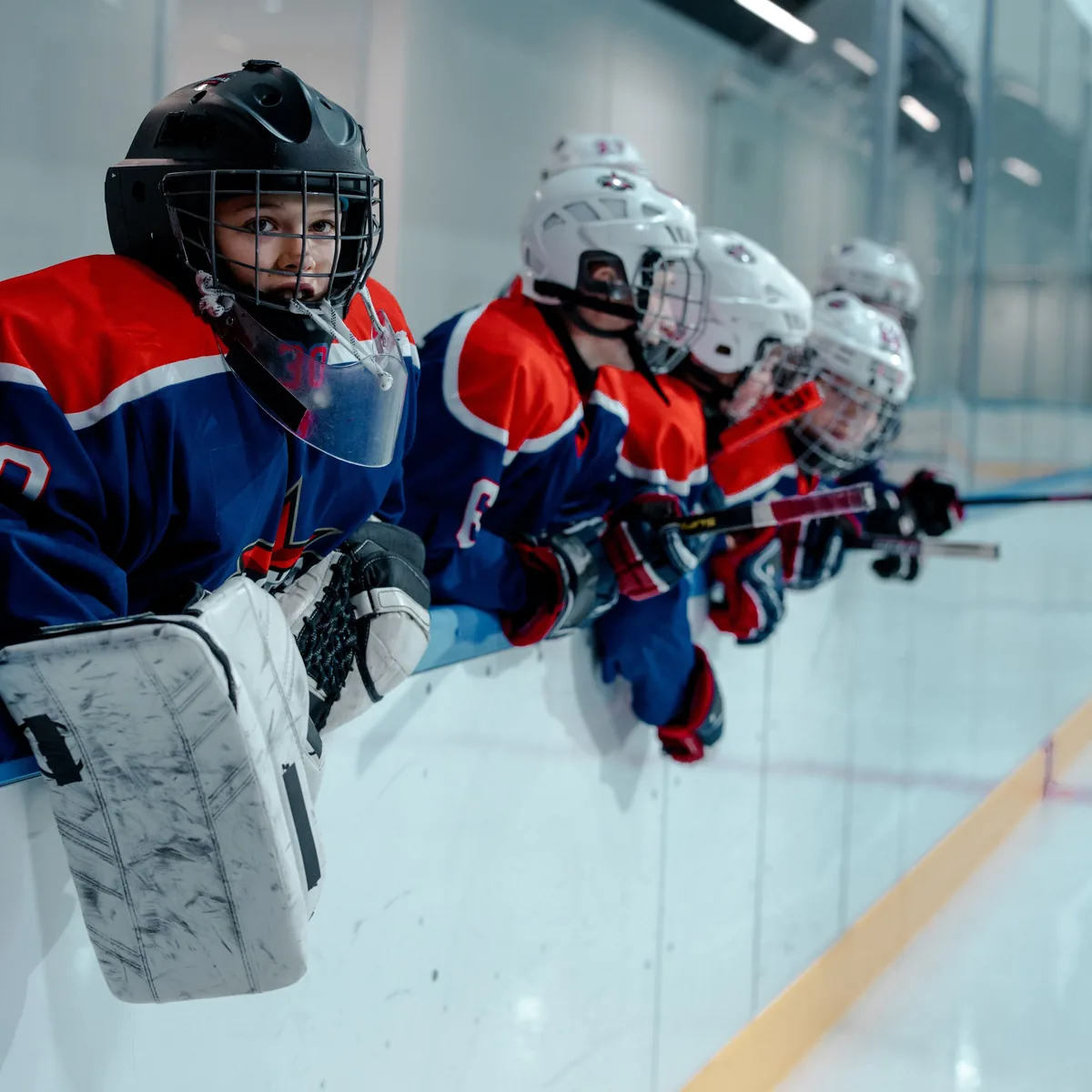 Young hockey players in full gear leaning on the boards, waiting for their shift